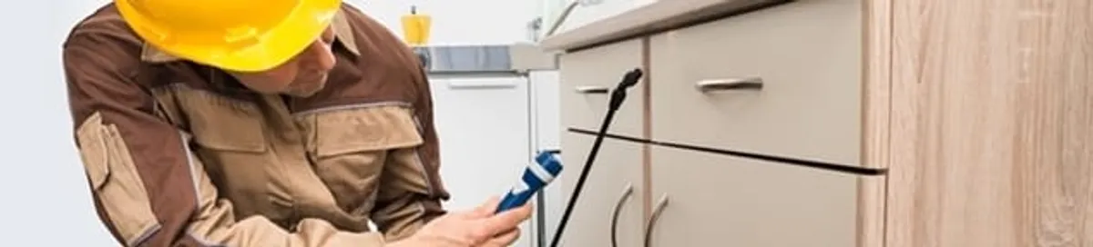 Roach exterminator applying treatment under kitchen cabinets in El Paso, TX