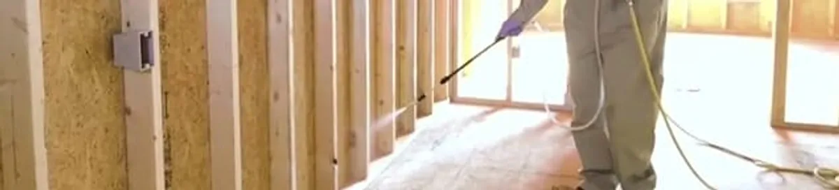 Termite treatment technician applying spray along framing and unfinished walls in El Paso, TX